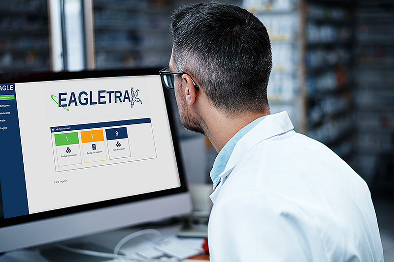 Pharmacist sitting in front of a computer displaying the EagleTrax homepage.