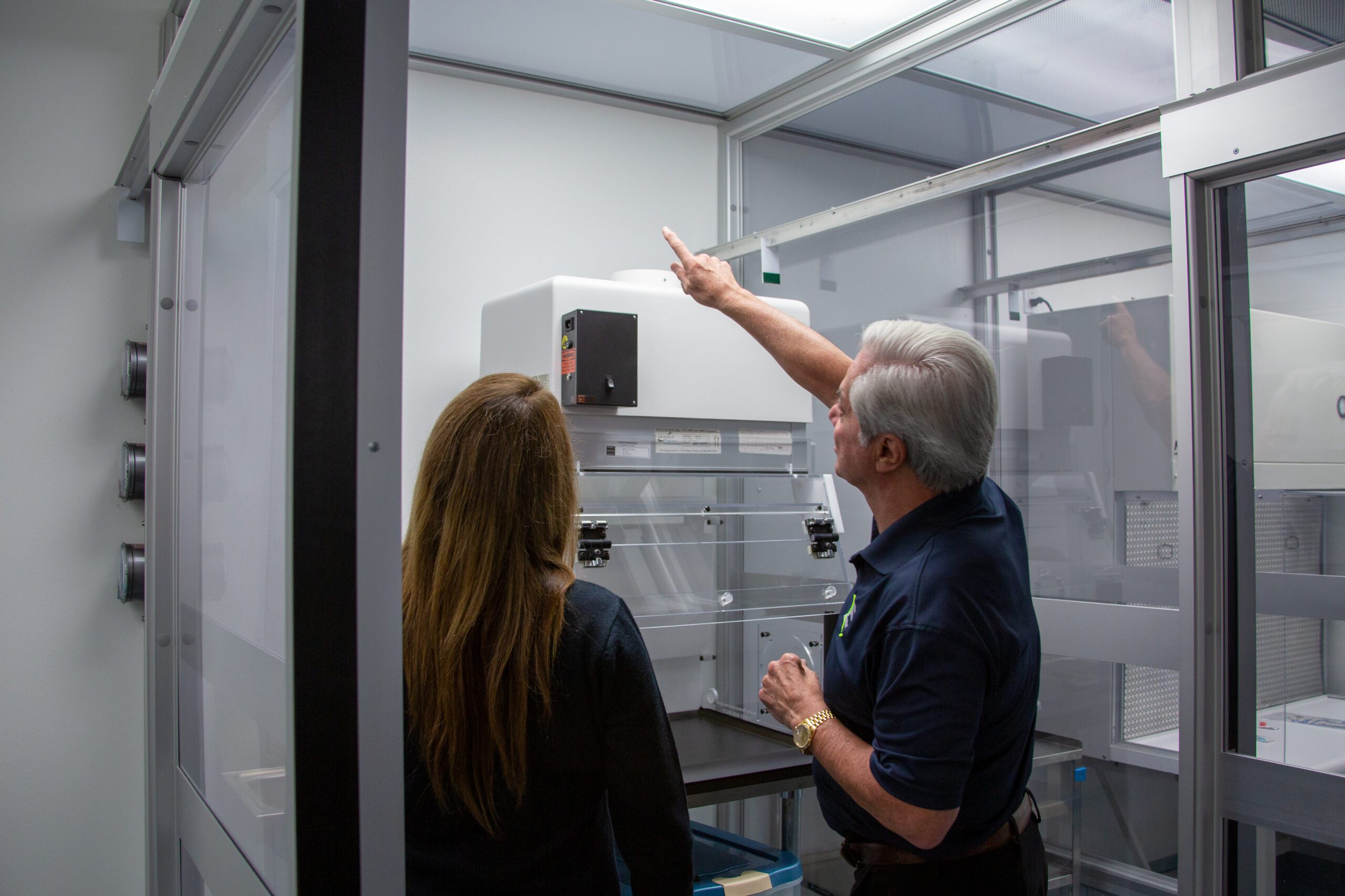 Image of an inspection taking place inside a pharmaceutical compounding lab. One person is pointing upwards towards an unseen object while another person looks on. The image features a caption stating, “Compliance Through Science – Eagle Consulting Services.”