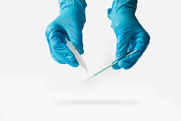 Lab gloved hands, one holding a single-use vial of sterile water and the other a swab for sampling.